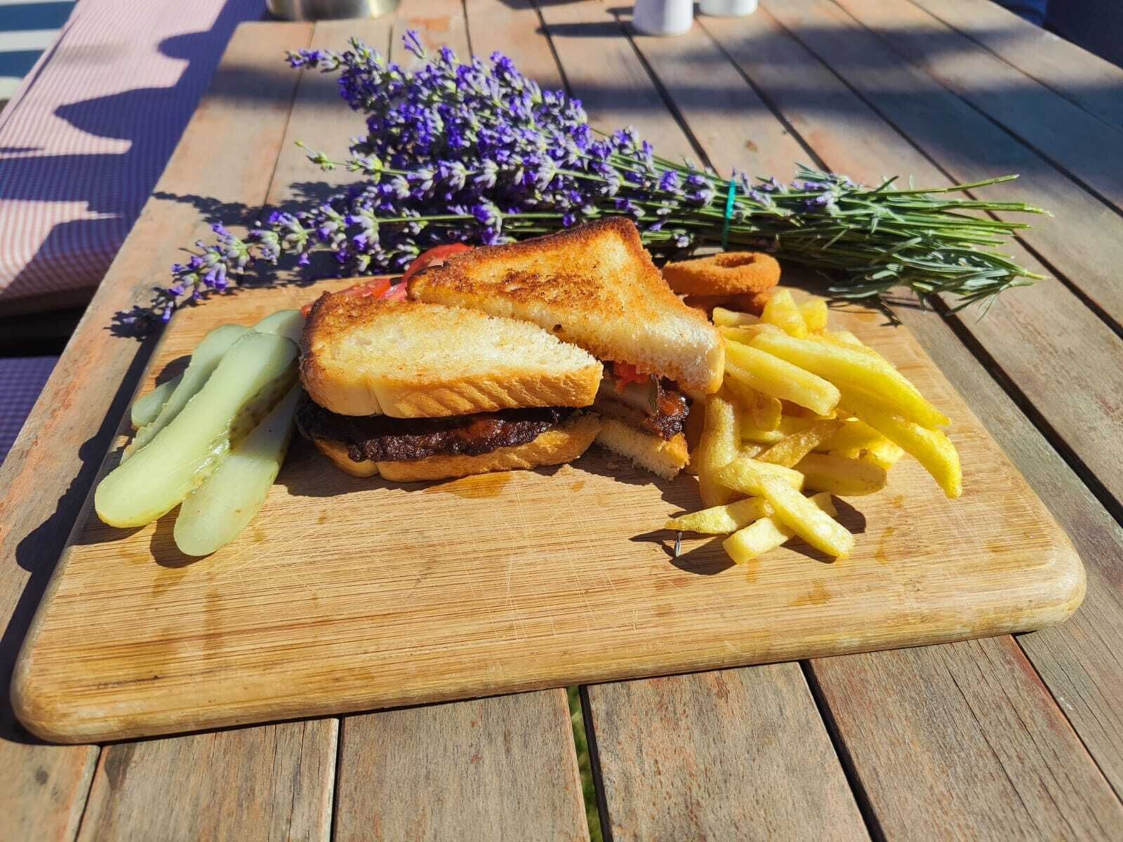 Un plato con un sándwich a la parrilla, papas fritas, pepinillos en vinagre y una ramita de romero sobre una mesa de madera.