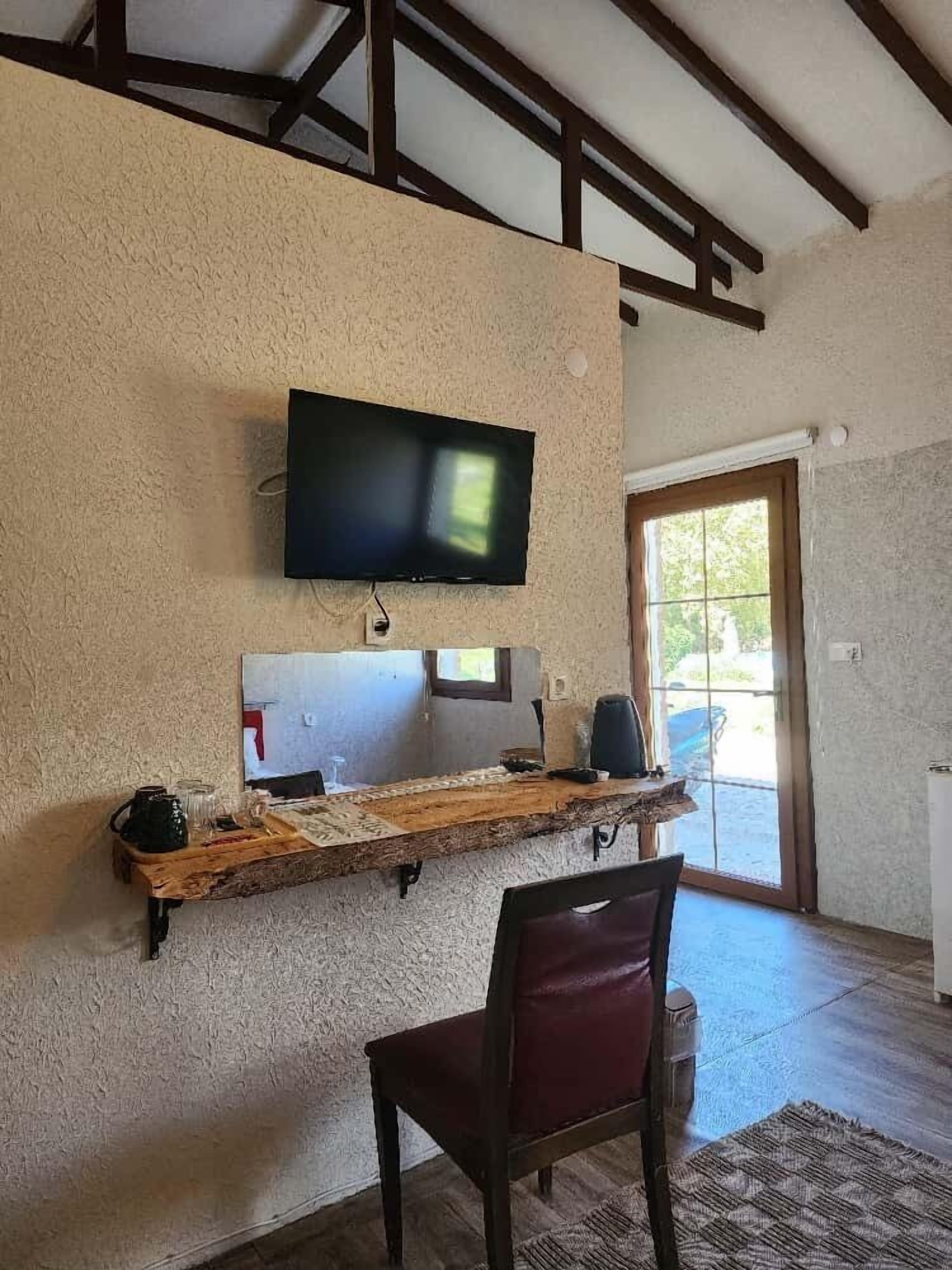 Habitación con televisor montado en una pared texturizada, un estante de madera con diversos objetos, una silla roja y una puerta que da al exterior.