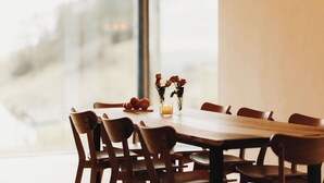 Un coin repas avec une table et des chaises en bois, un vase contenant des fleurs séchées et une bougie posée sur la table.