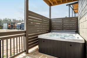 A hot tub in a covered outdoor area with wooden slats and a view of modern buildings in the background. - Twilight Mist Getaway | Pool, Hot Tub + Game Room! (Pigeon Forge)