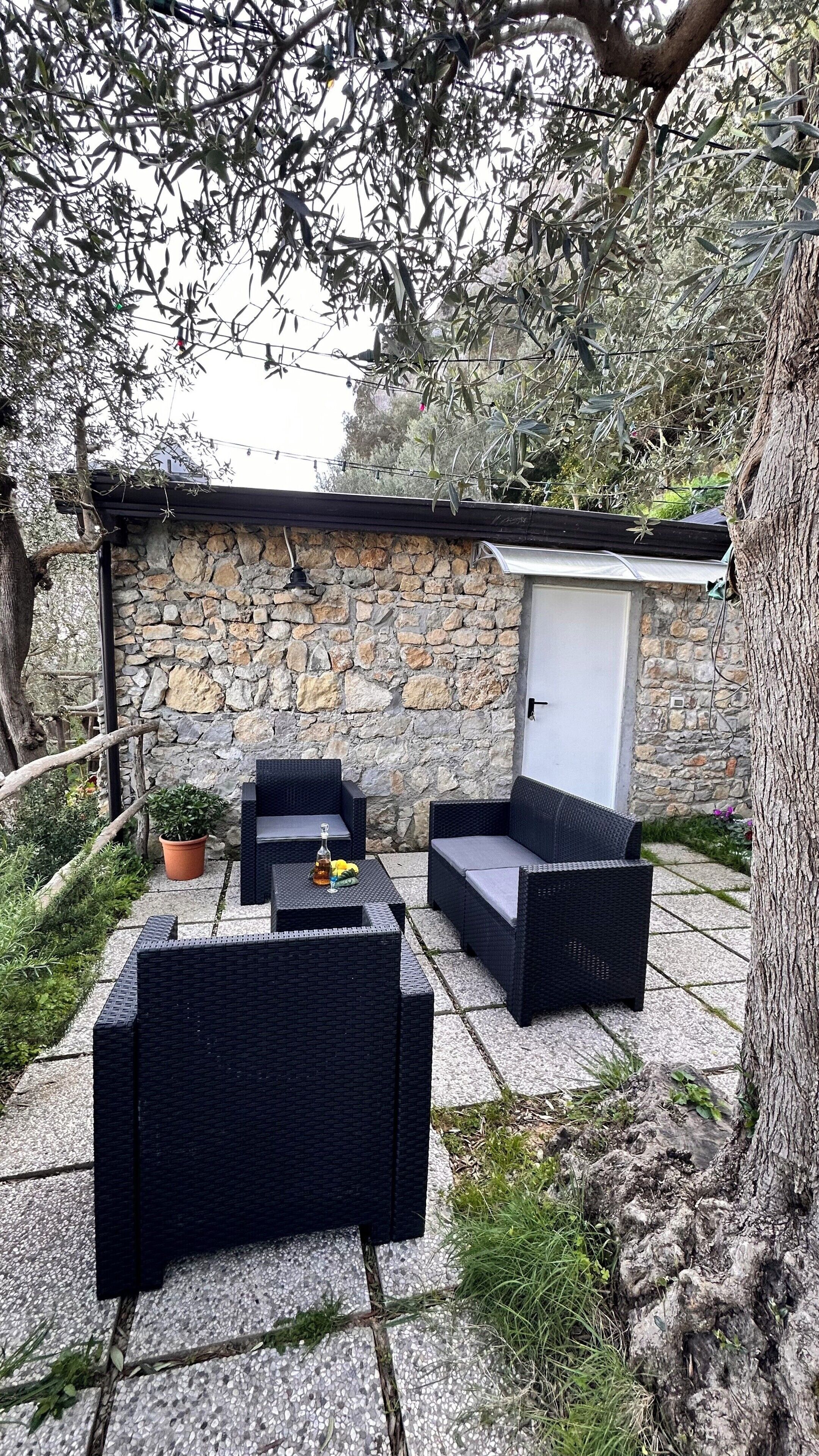 Un área de estar al aire libre con mobiliario de mimbre, un muro de piedra y una puerta.