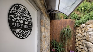 A sign with "AURY HOUSE" on a white wall, a stone wall, and a wooden fence with plants.