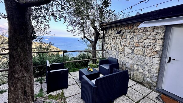A stone-walled outdoor area with wicker furniture and a view of the sea.