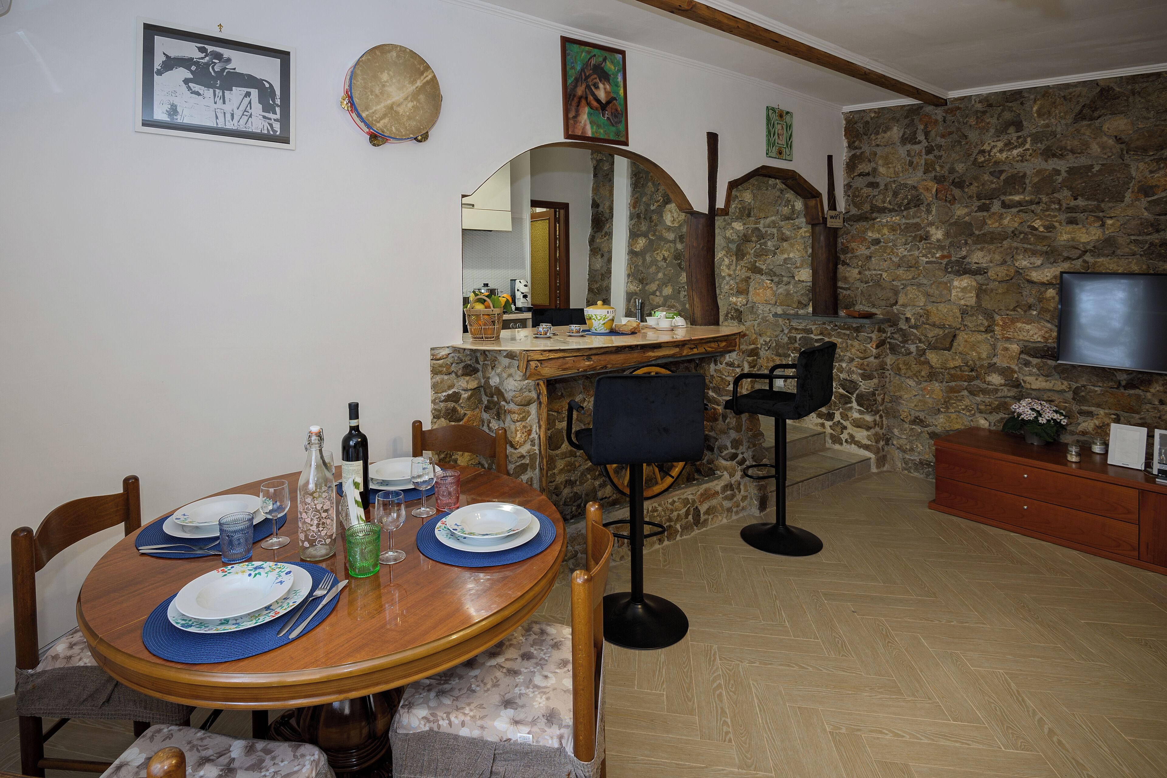 A dining area with a stone wall, wooden table, chairs, and a TV mounted on the wall.