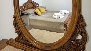 A bedroom with a large ornate mirror, a bed with a headboard, and a wall with a sunset painting.