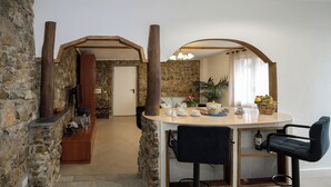 A stone-walled room with a wooden reception desk, a round bar area with two black barstools, and a potted plant.