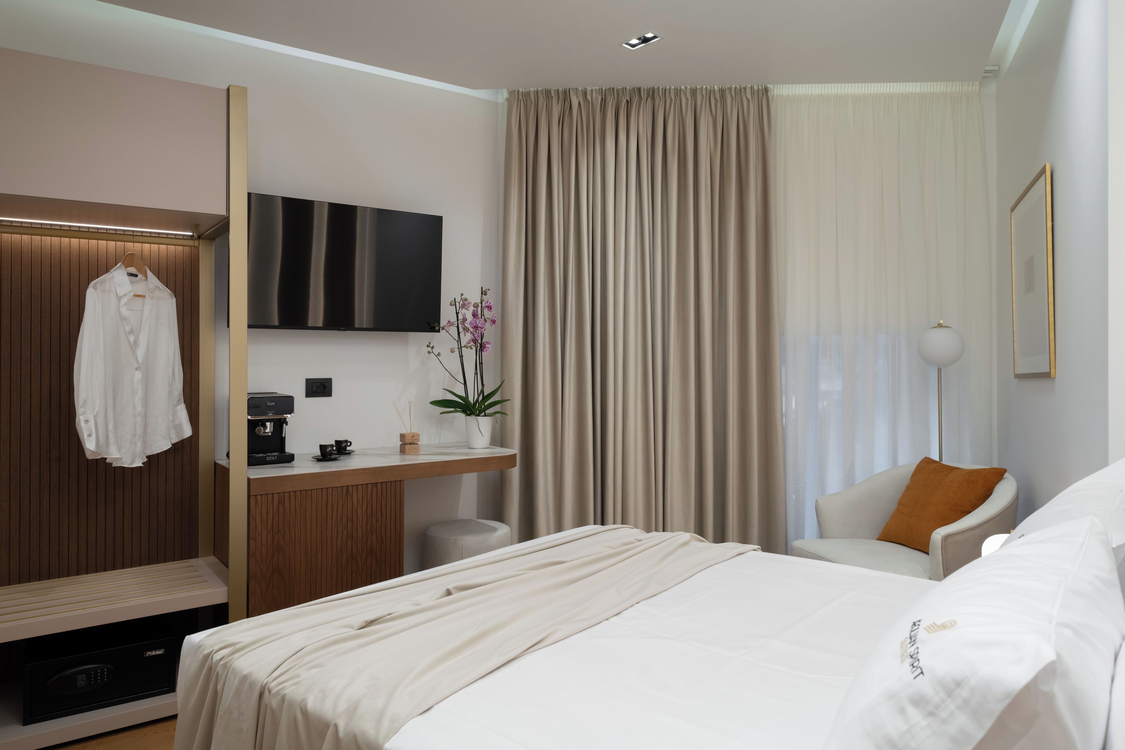 A modern hotel room with a large bed, a desk with a coffee machine, a TV, and a plant.