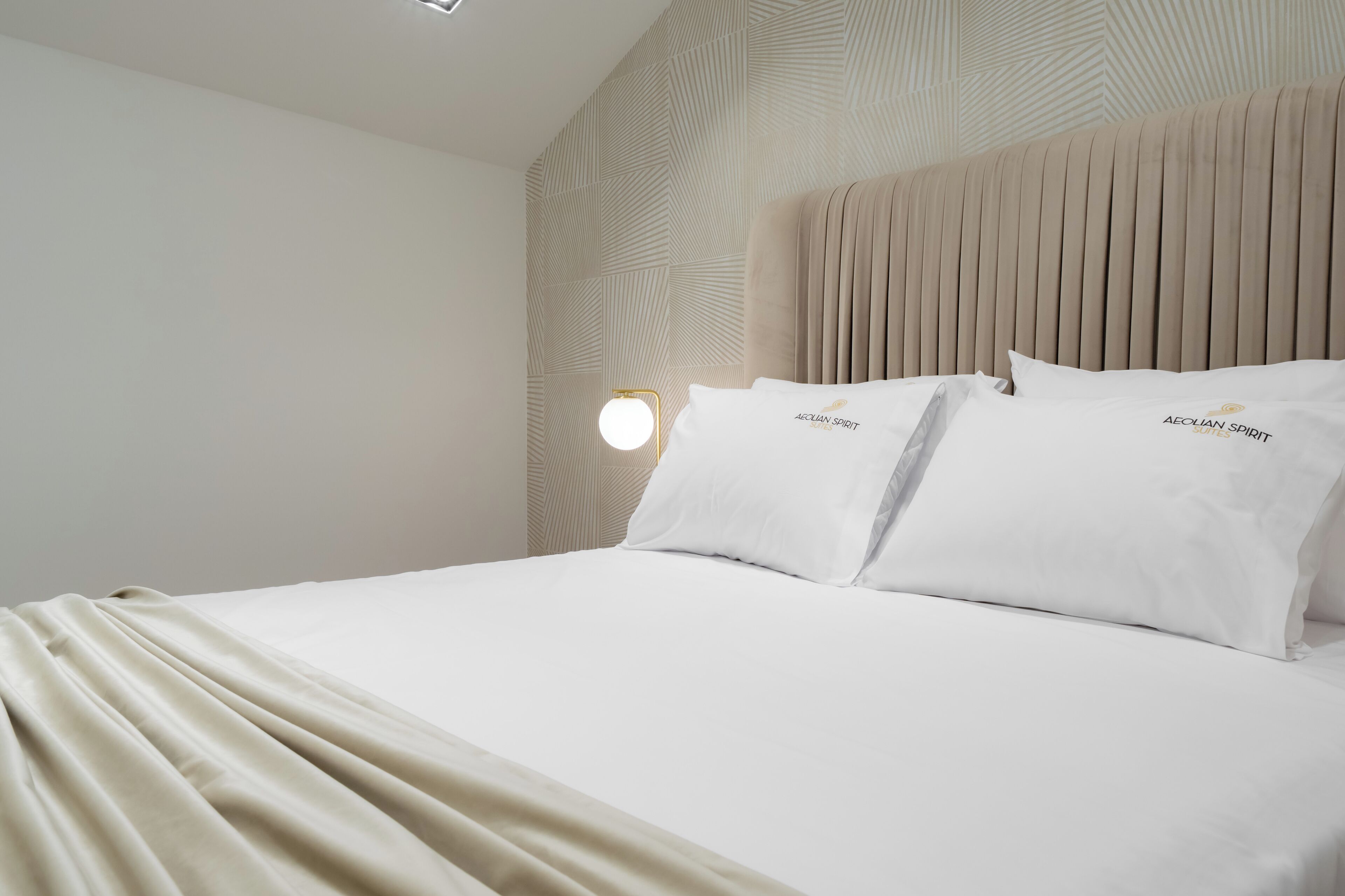 Una cama bien hecha con sábanas blancas y dos almohadas con la etiqueta 'AEQUIAN SPIRIT'.