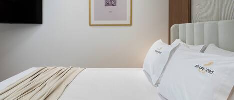 A hotel room with a bed, a framed picture on the wall, and a television mounted above it.