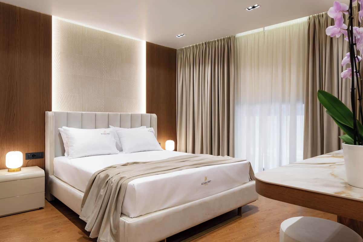 Une chambre d’hôtel moderne avec un grand lit, des tables de chevet, une table surmontée d’un plateau en marbre et une plante en pot.