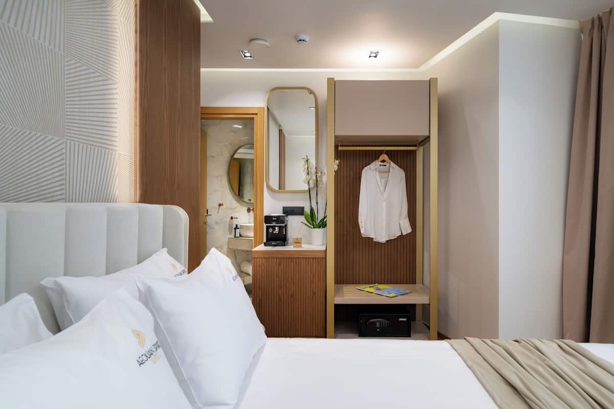 Une chambre d’hôtel comprenant un lit, une table de chevet en bois, un miroir, un peignoir et un petit bureau avec une machine à café.