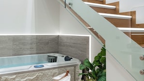 Un intérieur moderne avec un escalier à garde-corps en verre, un bain à remous et un fauteuil blanc.