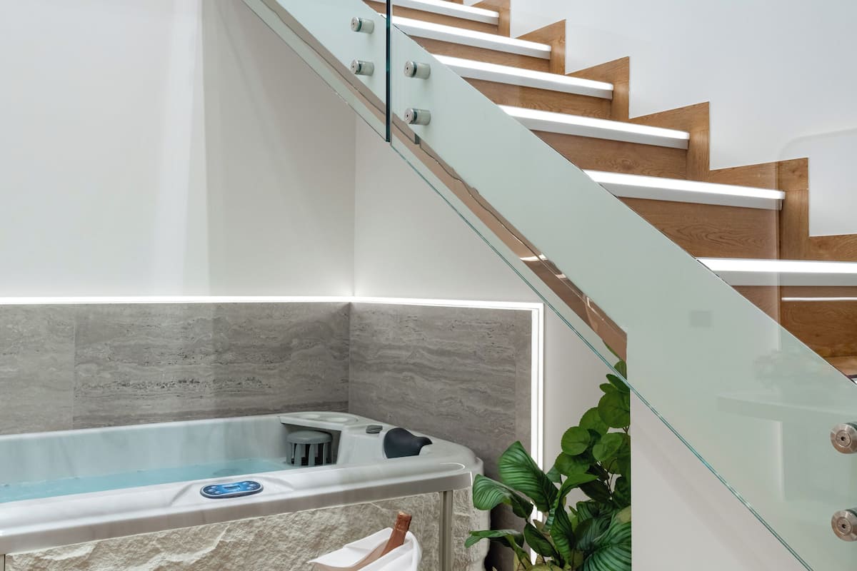 Un intérieur moderne avec un escalier à garde-corps en verre, un bain à remous et un fauteuil blanc.