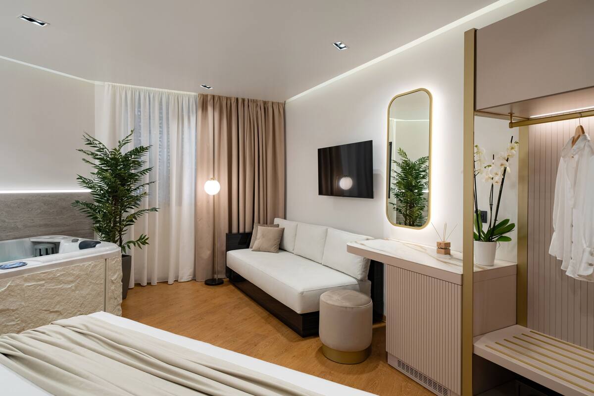Une chambre d’hôtel moderne équipée d’un lit, d’un canapé, d’une petite table, d’un miroir, d’une plante et d’une baignoire.