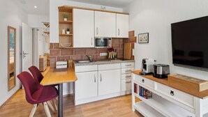 A compact kitchen with white cabinets, a microwave, and a coffee maker. There is a dining table with two chairs and a TV mounted on the wall. - Charysma: Rosso suite | warm & stylish design | terrace | parking lot (Hameln)