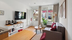 A modern living room with a flat-screen TV, a wooden dining table, a sofa, and a small side table. - Charysma: Rosso suite | warm & stylish design | terrace | parking lot (Hameln)
