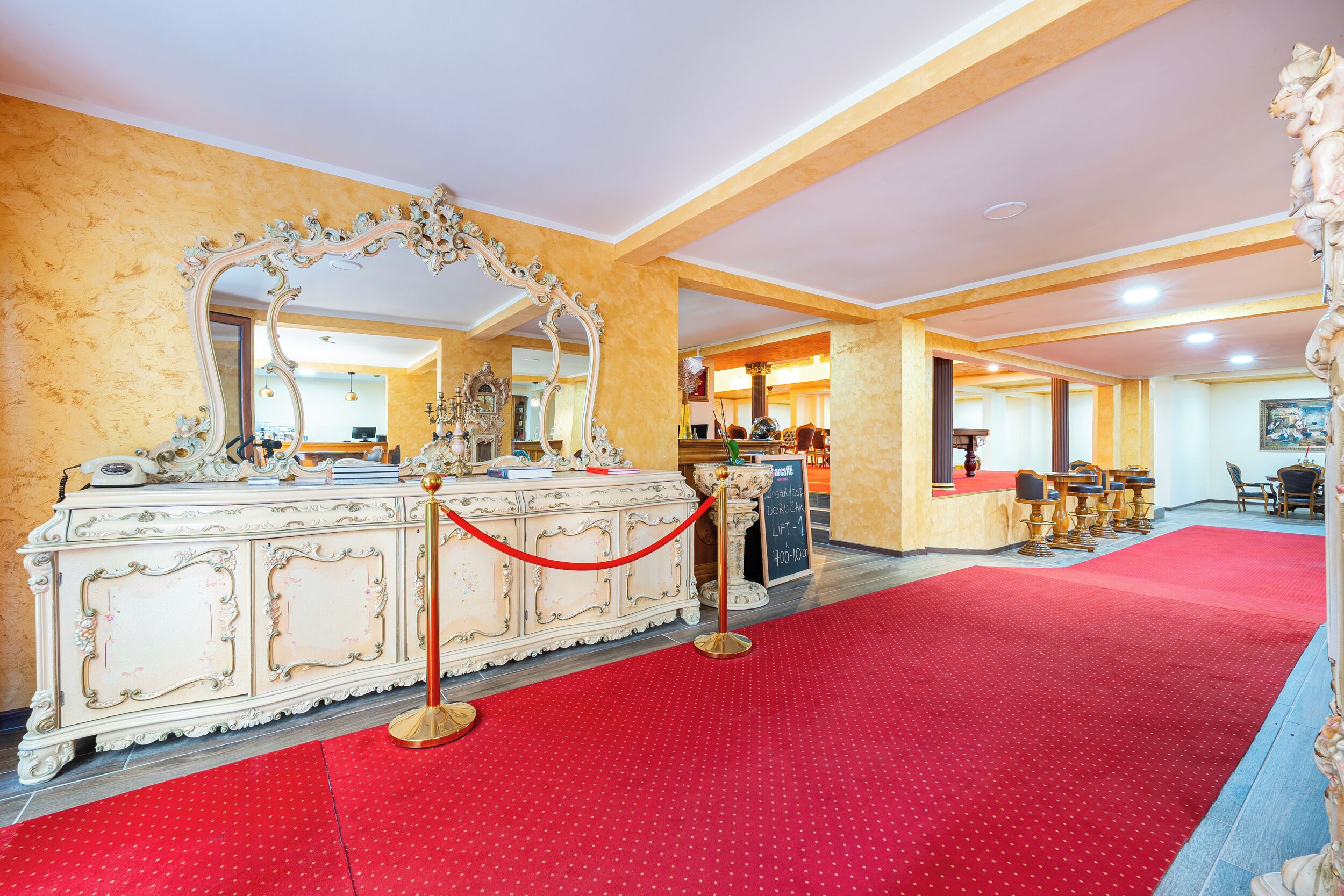 A hotel lobby with a red carpet, ornate white furniture, and a large mirror.