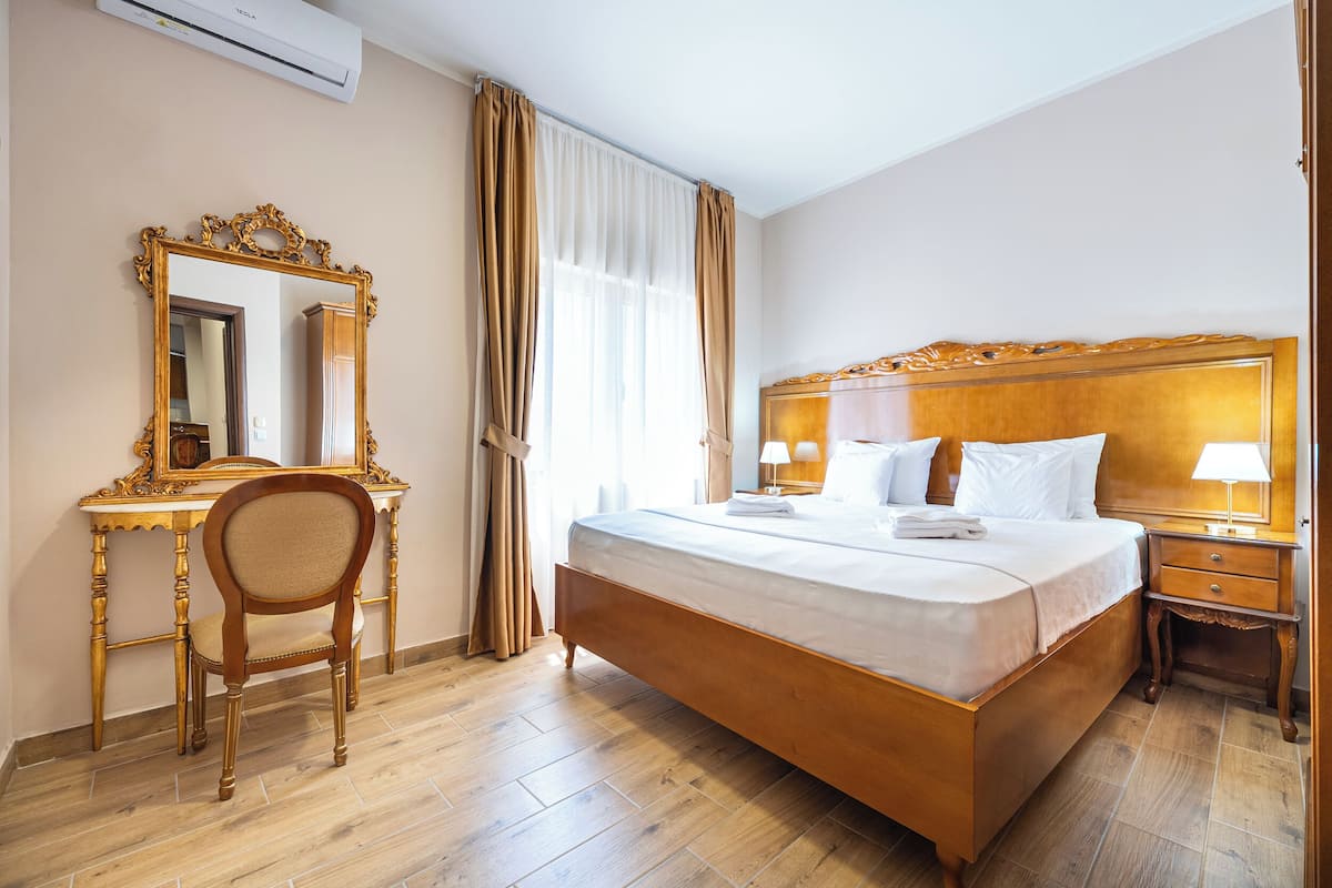 A hotel room with a large bed, a wooden desk, a chair, a nightstand, and a mirror.