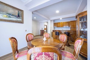 Un área de comedor con una mesa redonda de madera, seis sillas con tapicería estampada y un cuadro en la pared.