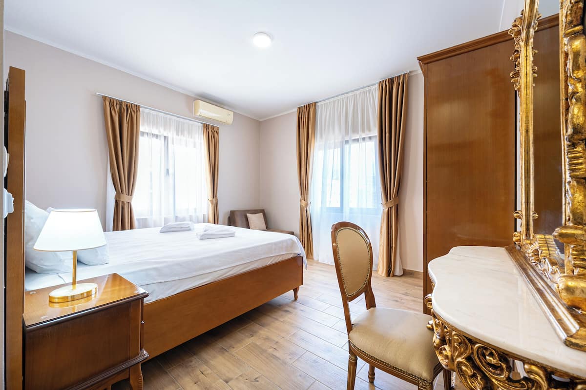 A hotel room with a bed, a chair, a vanity with a mirror, and curtains.