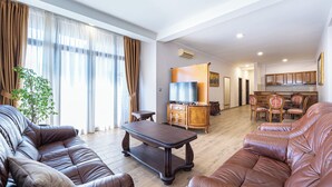 A living room with leather sofas, a wooden coffee table, and a dining area with a TV and wooden cabinets. - Hotel Perun (Budva)