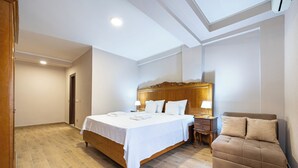 A bedroom with a wooden bed, a sofa, a nightstand, and a ceiling light. - Hotel Perun (Budva)
