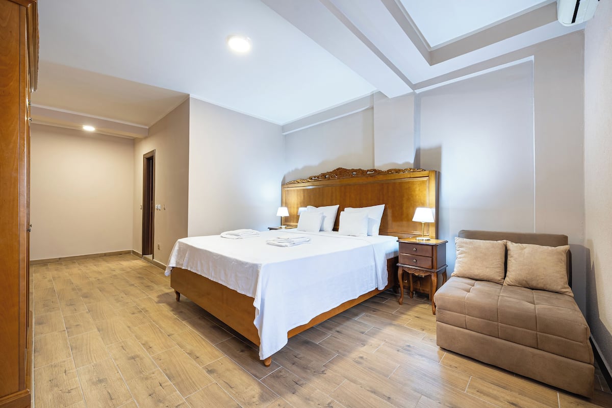 A bedroom with a wooden bed, a sofa, a nightstand, and a ceiling light.