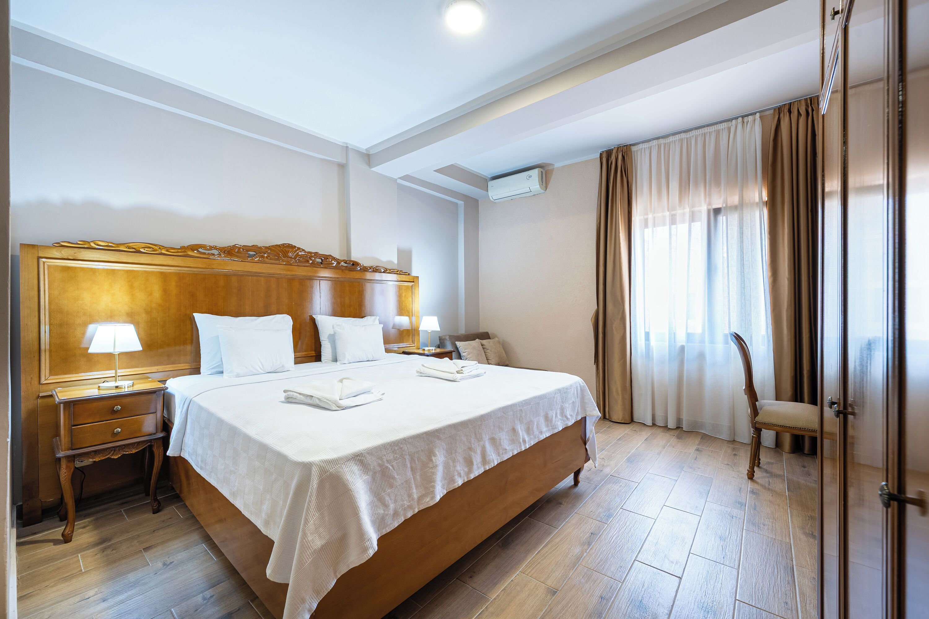 A hotel room with a large bed, bedside tables, a lamp, a chair, and a wardrobe.