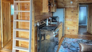 A rustic cabin interior with a wooden staircase, a kitchen with a stove and sink, and a living area with a couch. - New spacious-charming one bedroom cottage with loft at Wilson Lake Country Club (Wilton)