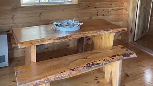 A rustic wooden cabin interior with a large window, a wooden table with a bowl, and a bench. - New spacious-charming one bedroom cottage with loft at Wilson Lake Country Club (Wilton)