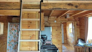 A rustic cabin interior with a wooden ceiling, a central staircase, a kitchen area, and a seating area with a leather couch. - New spacious-charming one bedroom cottage with loft at Wilson Lake Country Club (Wilton)