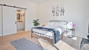 A modern bedroom with a metal bed frame, a bedside table with a lamp, a small potted plant, and a sliding door leading to a bathroom. - Stylish 3BR 2BA Urban Retreat Near Lively Downtown (San Antonio)