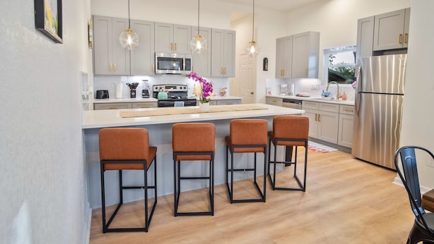 A modern kitchen with grey cabinets, a stainless steel refrigerator, and three bar stools. - Stylish 3BR 2BA Urban Retreat Near Lively Downtown (San Antonio)