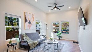 A modern living room with a grey sofa, a round coffee table, and a flat-screen TV mounted on the wall. - Stylish 3BR 2BA Urban Retreat Near Lively Downtown (San Antonio)