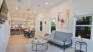 A modern living room with a grey sofa, a coffee table, and a dining area with chairs and a table. - Stylish 3BR 2BA Urban Retreat Near Lively Downtown (San Antonio)