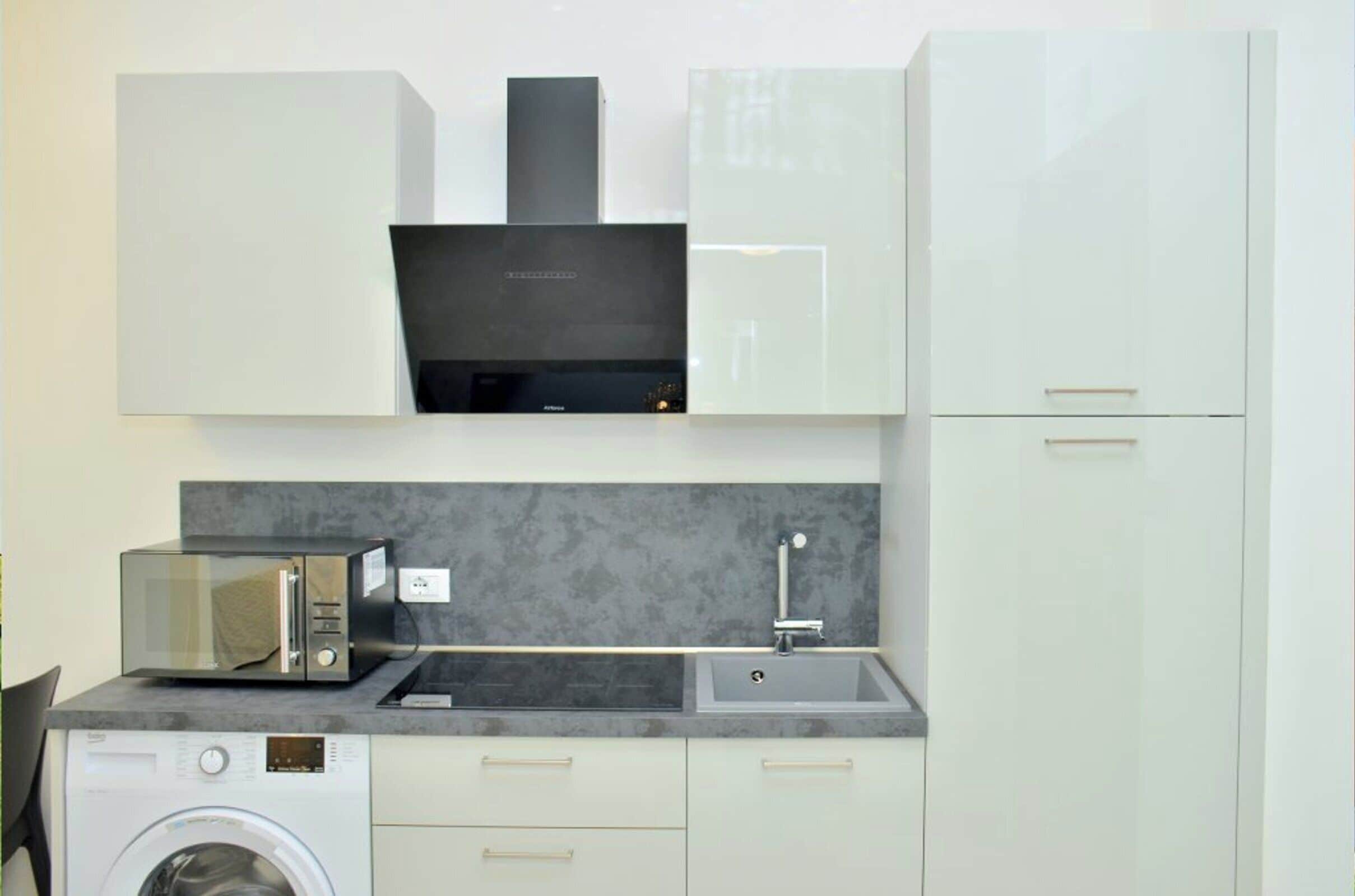 A compact kitchen with a washing machine, microwave, and sink.