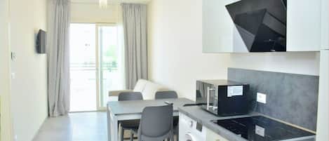 Une cuisine moderne équipée d’un four à micro-ondes, d’une cuisinière et d’un lave-linge intégrés. On y trouve un coin repas avec une table et des chaises, ainsi qu’une grande fenêtre avec des rideaux.