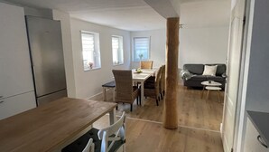 Ett modernt kök med ett träbord och stolar, en matplats med ett vitt bord och stolar samt ett vardagsrum med en soffa och ett soffbord.