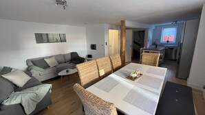 Ett modernt vardagsrum med en grå soffa, ett matbord med en vas och ett köksområde som syns i bakgrunden.
