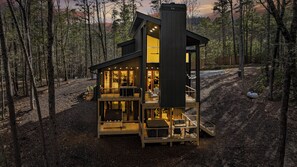 Une cabane moderne dotée d’une terrasse en bois, de plusieurs niveaux et d’une grande fenêtre.