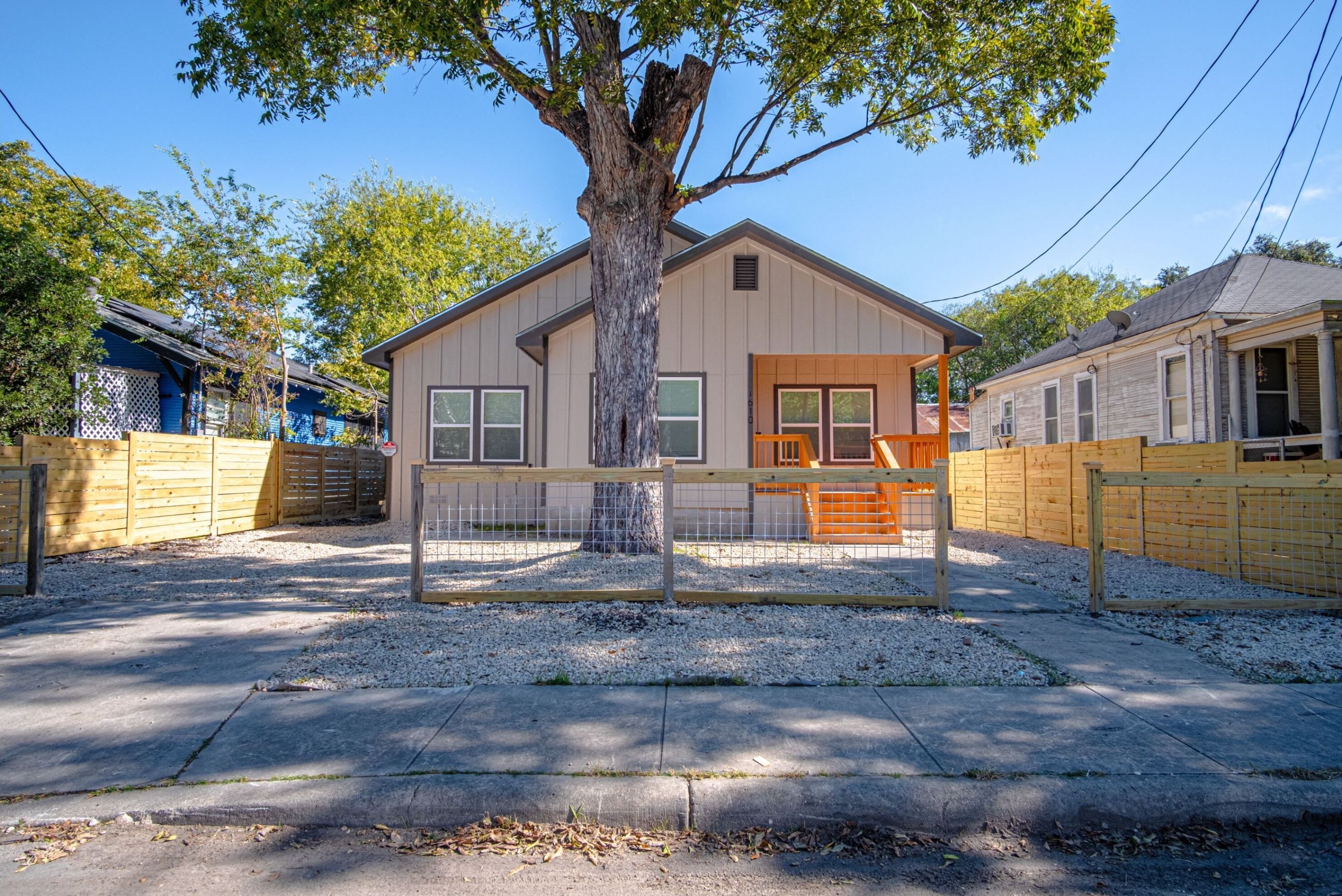 A single-story house with a fenced yard, a large tree in front, and a clear sky.