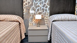 Et værelse med to senge, begge med stribet sengetøj, et natbord med lampe, og en væg med girafmønster.