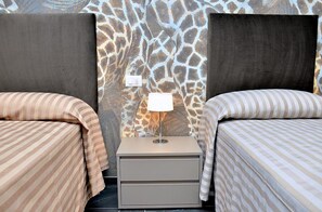 A room with two beds, each with striped bedding, a nightstand with a lamp, and a giraffe-patterned wall. - Charming Apartment With Sea-view Terrace (San Michele al Tagliamento)