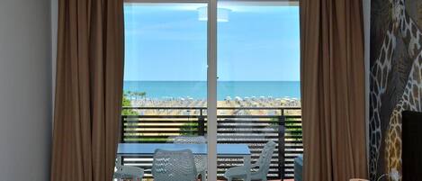 A hotel room with a large sliding glass door leading to a balcony with a view of the beach and ocean.