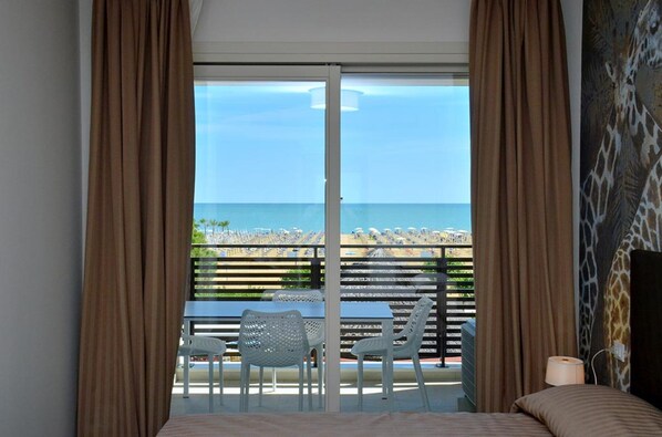 A hotel room with a large sliding glass door leading to a balcony with a view of the beach and ocean.