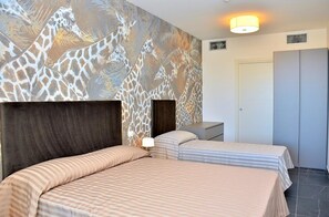 A hotel room with two beds, a giraffe mural on the wall, a bedside table with a lamp, and a wardrobe.