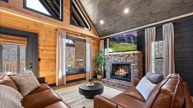 A cozy living room with a stone fireplace, leather sofas, and a large TV screen. - Luxury Cabin: Views, Theater, Hot Tub & Games (Sevierville)