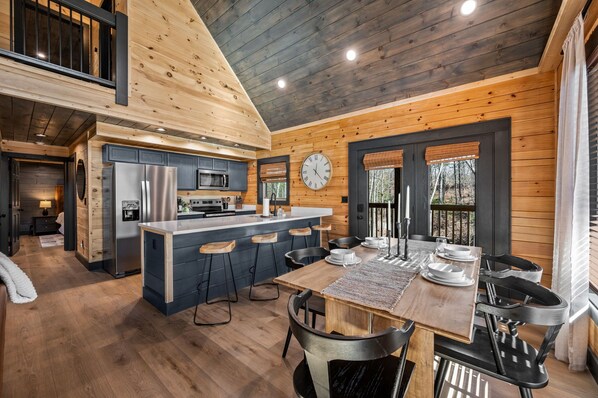 A modern kitchen with a central island, dark cabinetry, and a large clock on the wall.