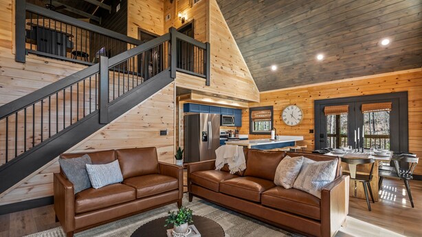 A spacious living area with a staircase, wooden walls, a kitchen, and a dining area. - Luxury Cabin: Fireplace, Theater, Hot Tub & Games (Sevierville)
