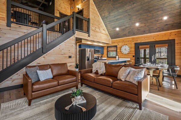 A spacious living area with a staircase, wooden walls, a kitchen, and a dining area.